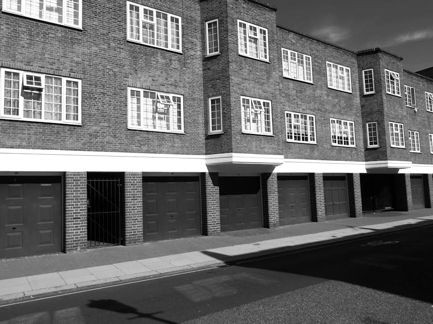Close-up view of the exterior of a multi-storey residential building with multiple balconies. The concrete facade shows a uniform pattern of rectangular balconies with white railings, some of which ha